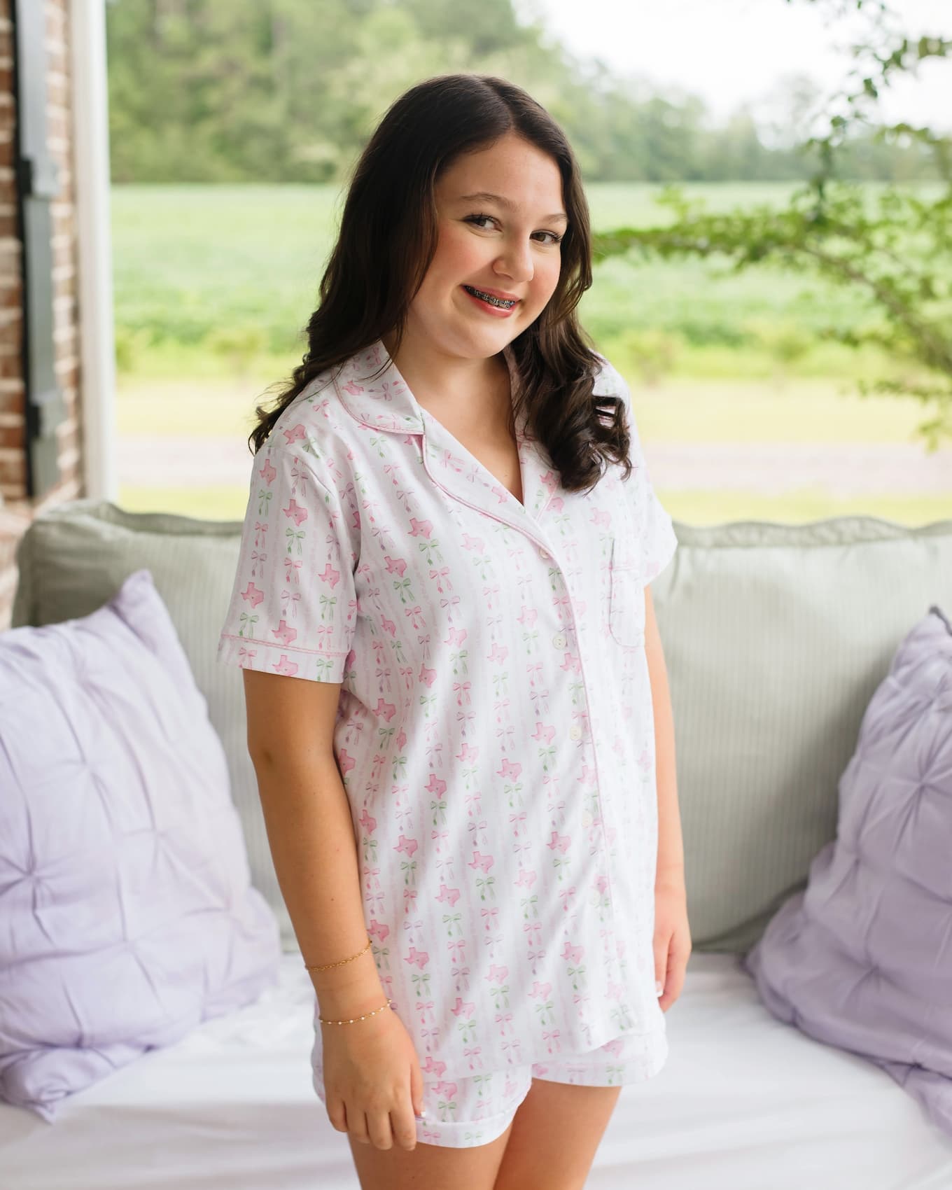Woman wearing a light pink pajama top with a floral pattern in a bright room.