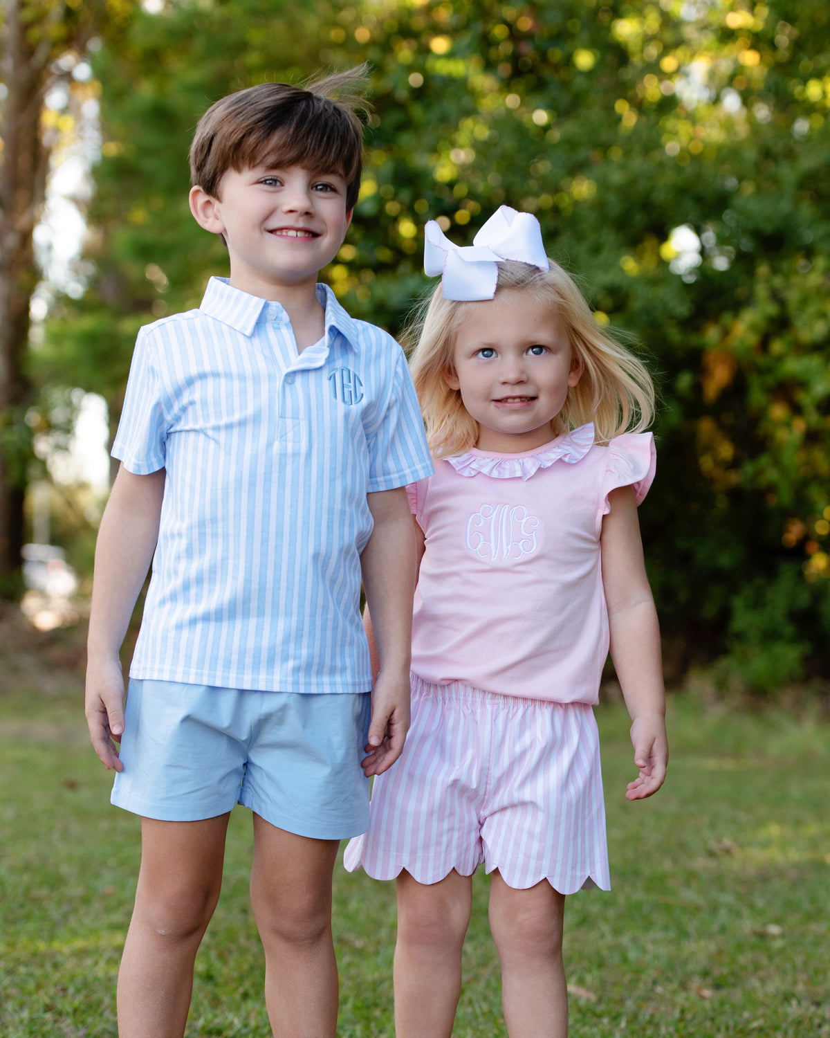 Young boy and girl standing outside wearing matching blue and pink striped outfits