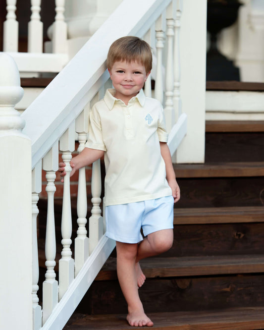 Young boy in a light-colored shirt and shorts standing on a staircase.