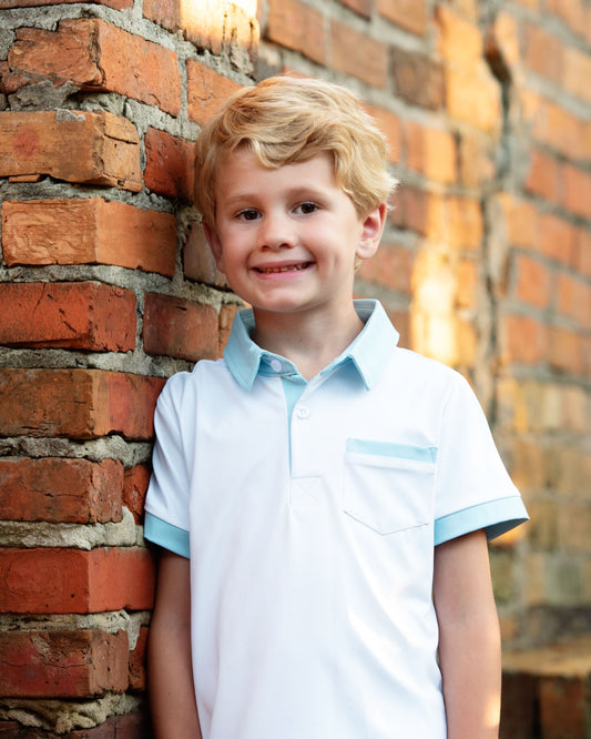 Young_boy_in_a_light_blue_shirt_standing_against_a_brick_wall