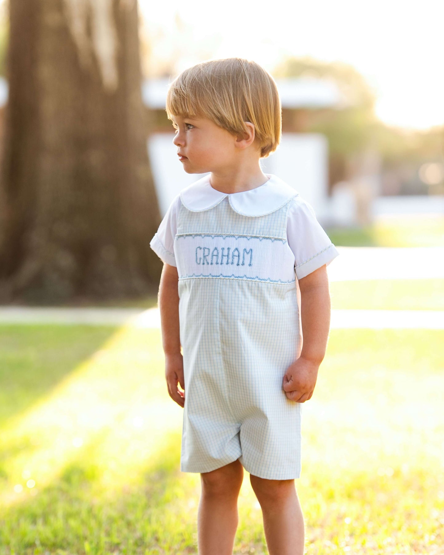 Young boy in a white outfit with 'Graham' embroidered outdoors