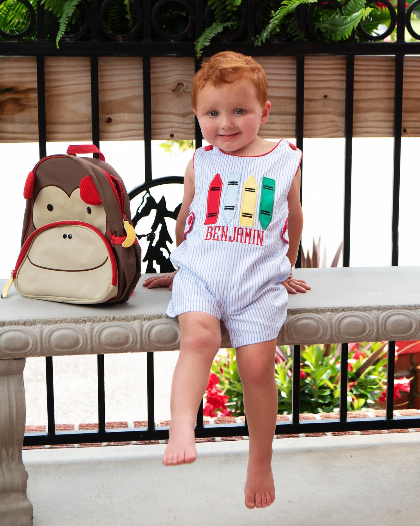 Young boy sitting on a bench next to a monkey backpack wearing a crayon outfit
