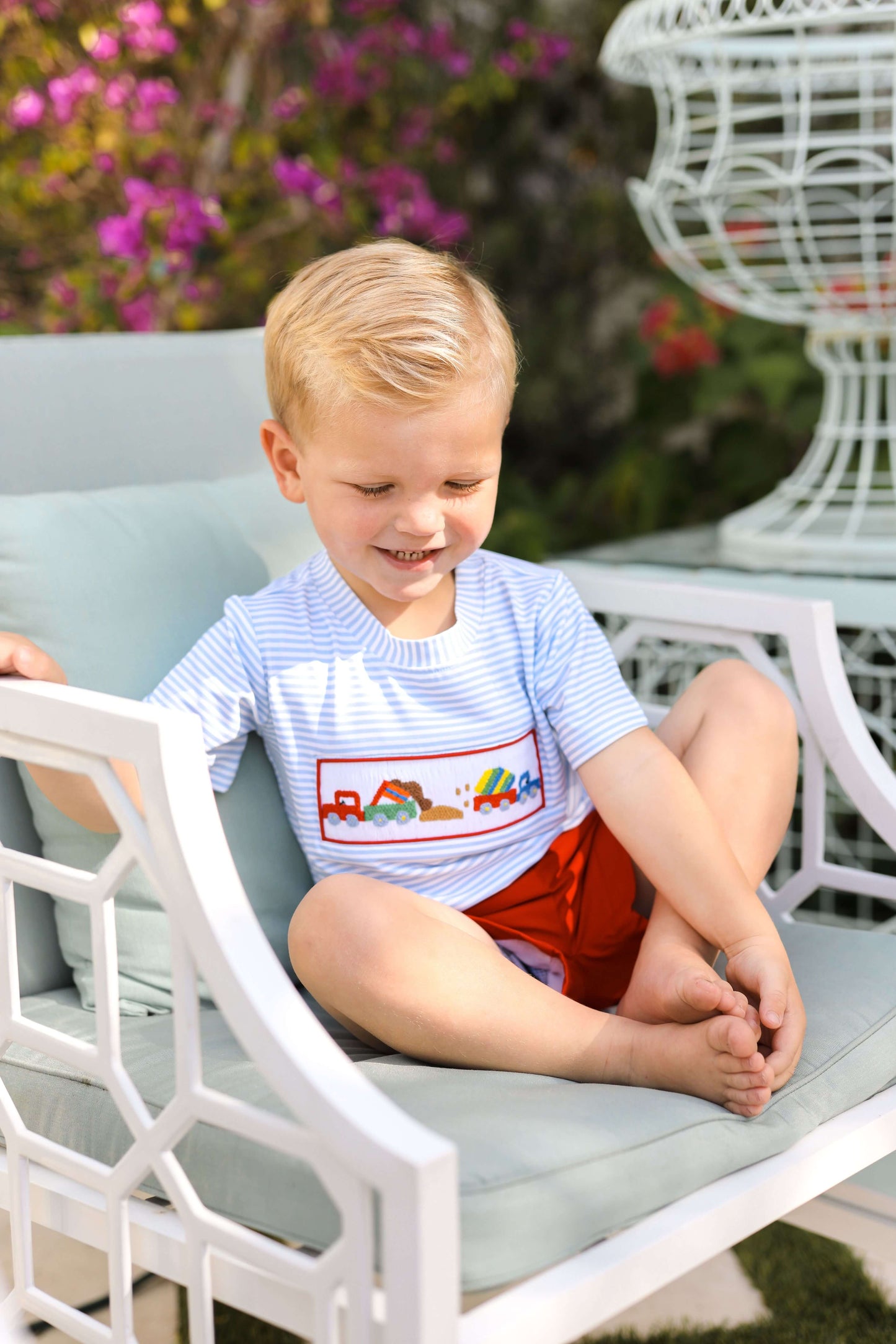 Young boy sitting on a white chair outdoors with flowers in the background