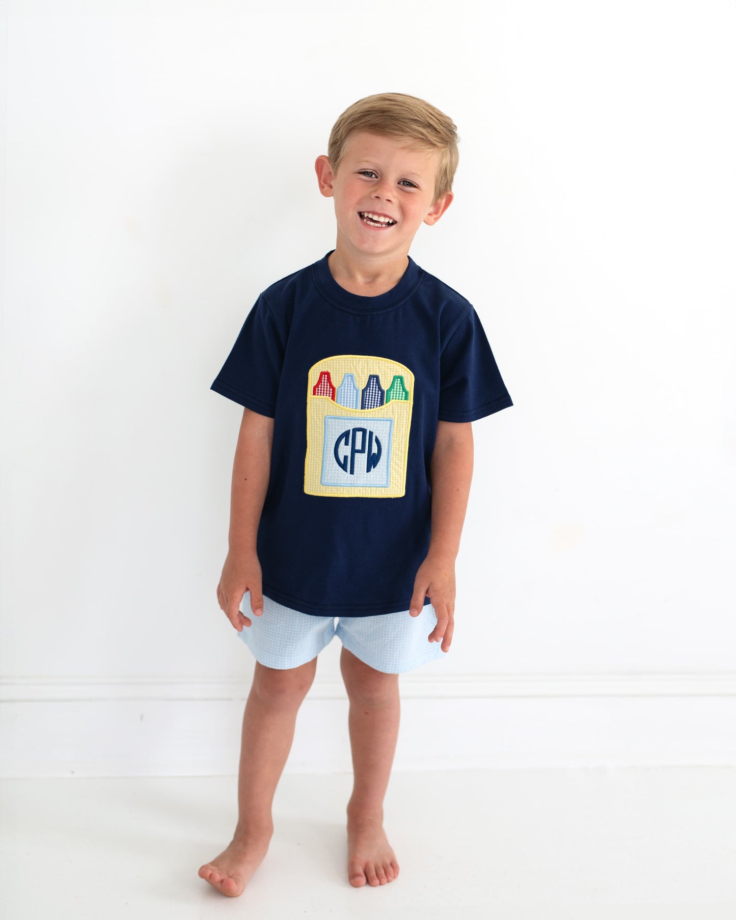 Young boy smiling wearing a school outfit with a crayon box and a monogram.