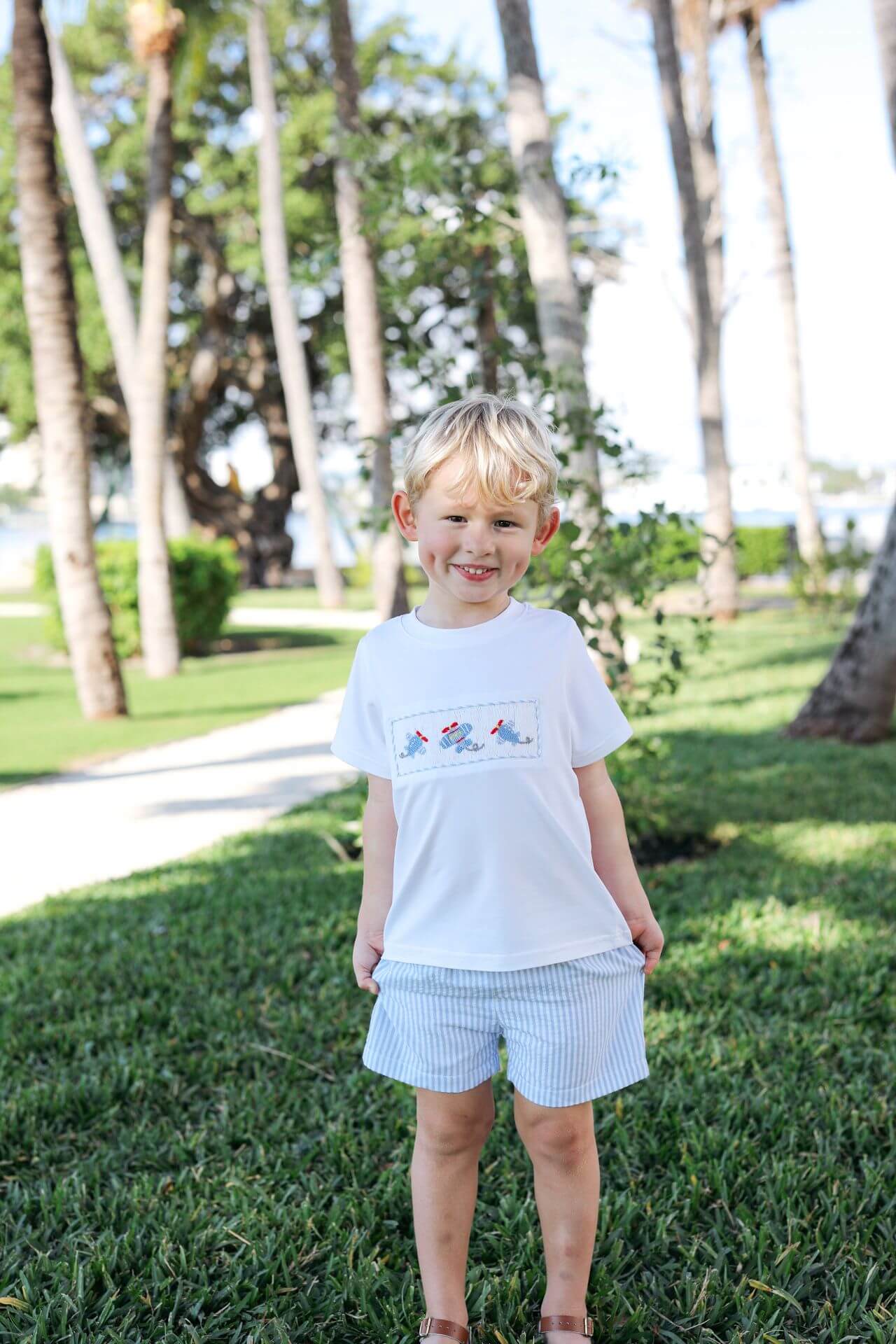 Young boy standing on grass with palm trees in the background