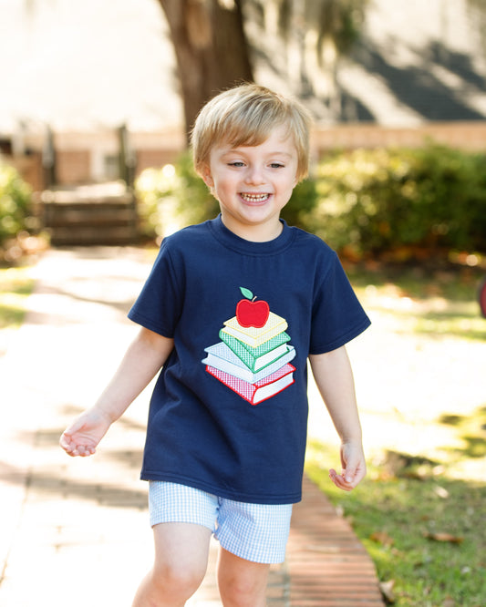 Young boy walking wearing a shirt with books and an apple.