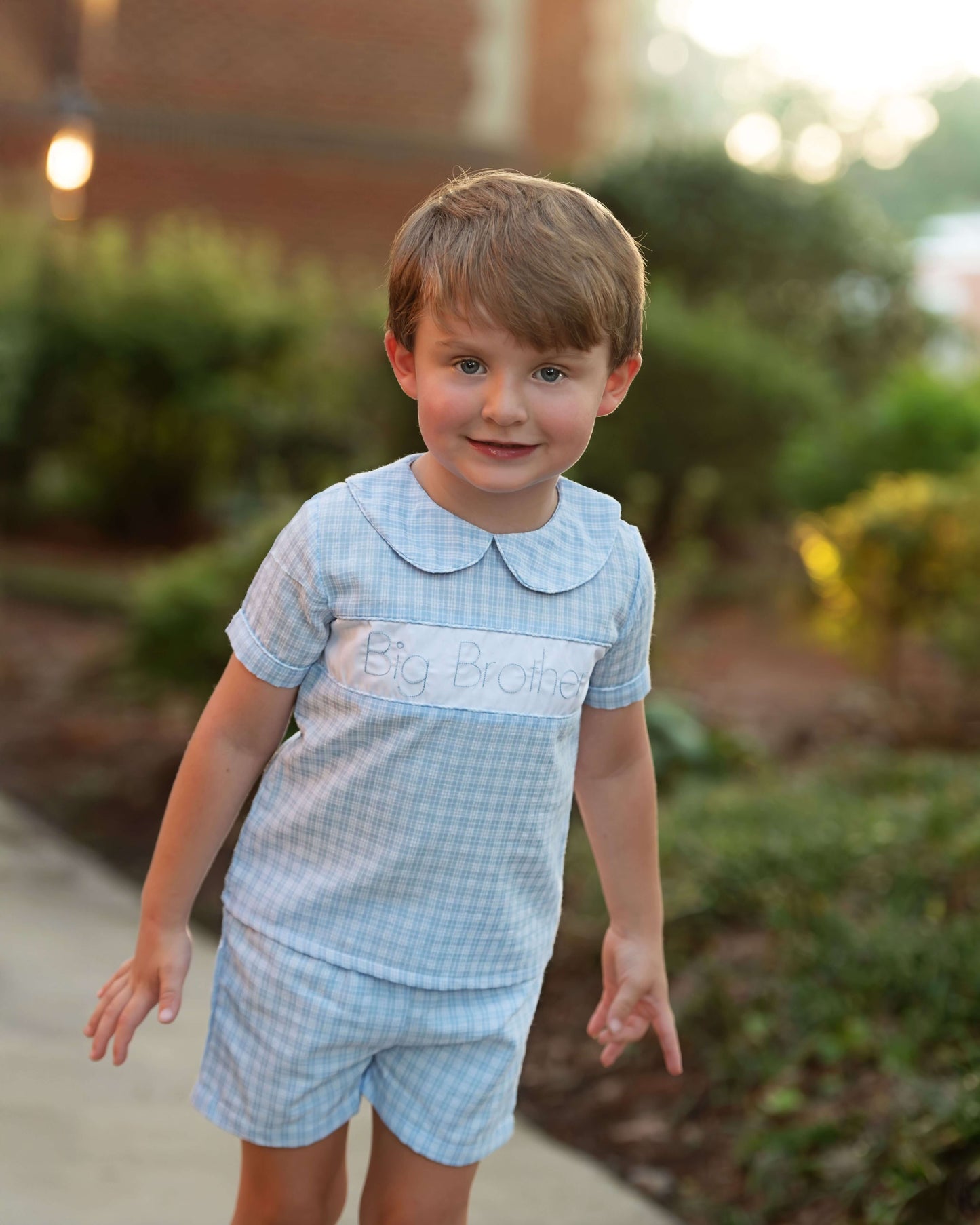 Young boy wearing a 'Big Brother' outfit outdoors with greenery in the background