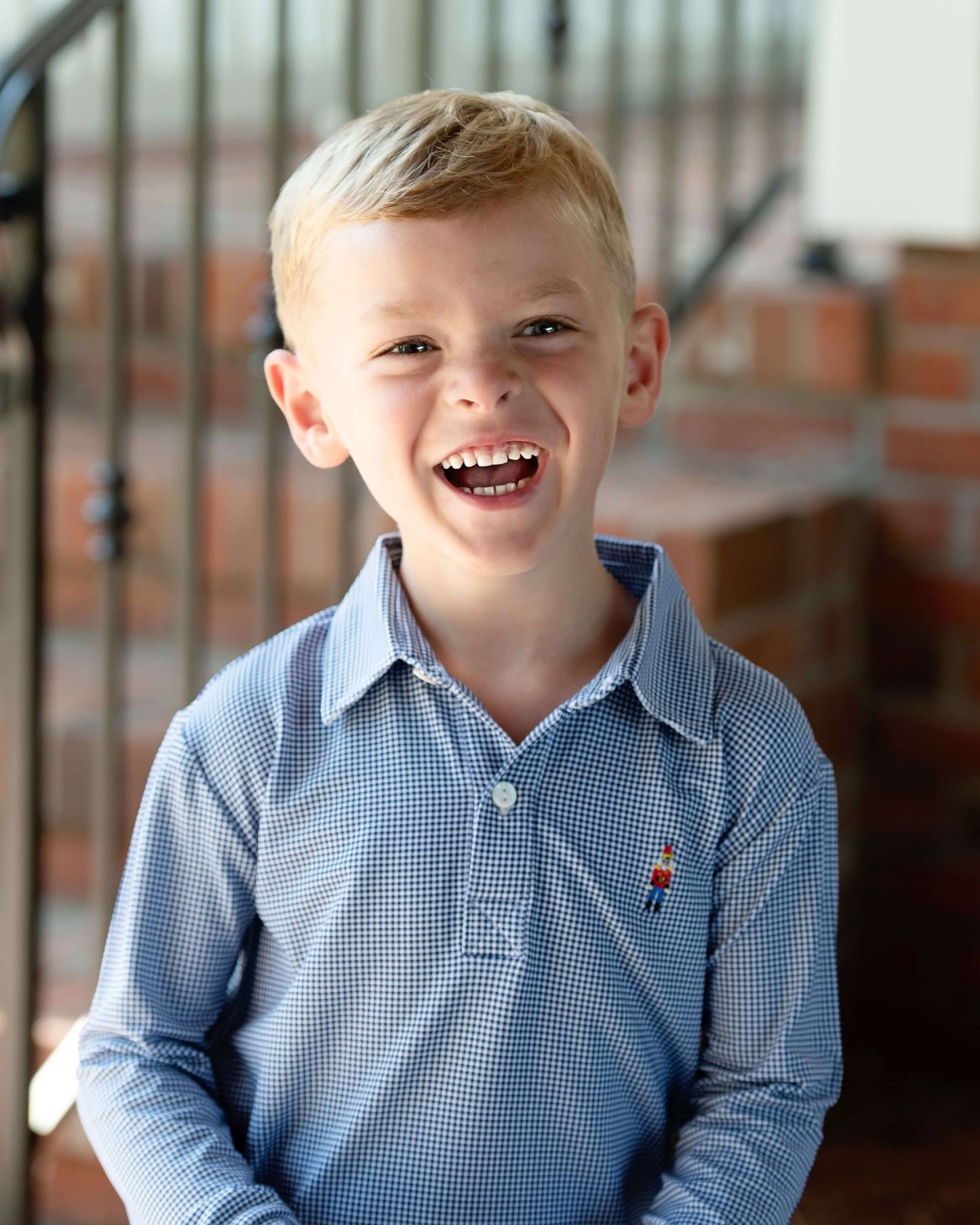 Young boy wearing a blue gingham shirt with a nutcracker, standing indoors.