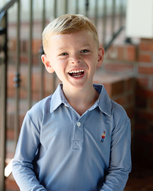 Young boy wearing a blue gingham shirt with a nutcracker, standing indoors.