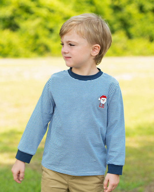 Young boy wearing a blue striped shirt with a red character on it, standing in a grassy field.