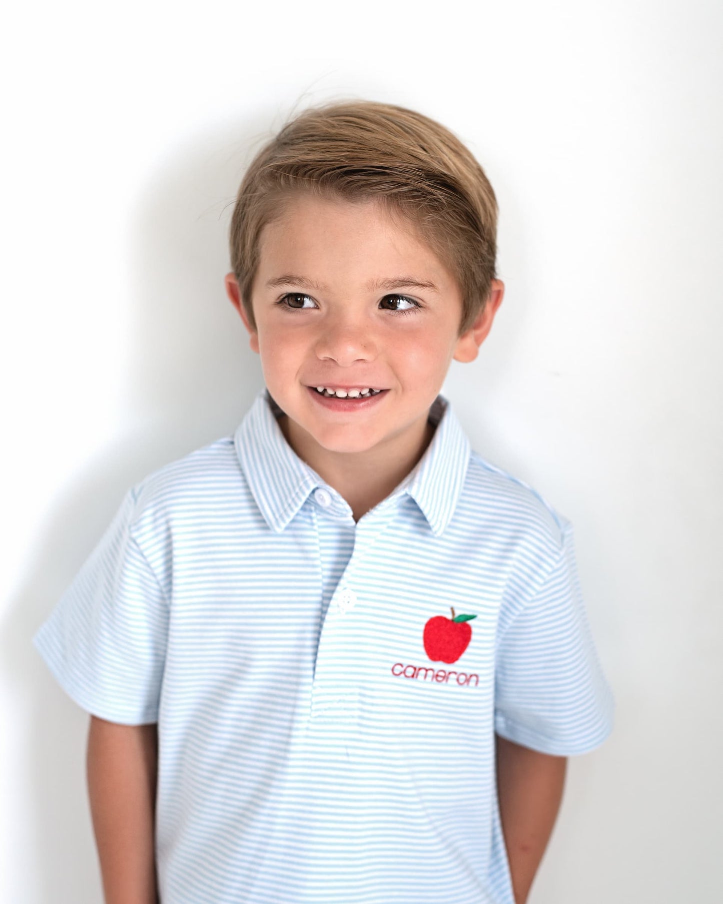 Young boy wearing a blue striped shirt with an apple embroidered.