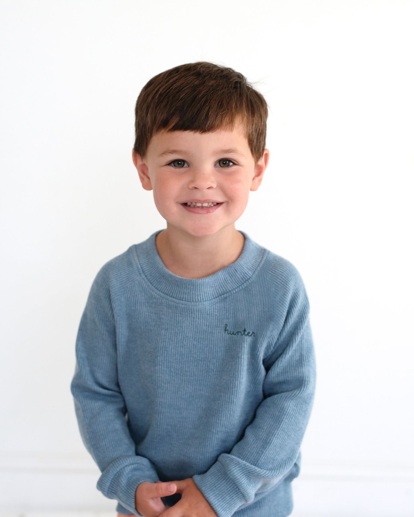 Young boy wearing a blue sweater with a brand logo on a white background