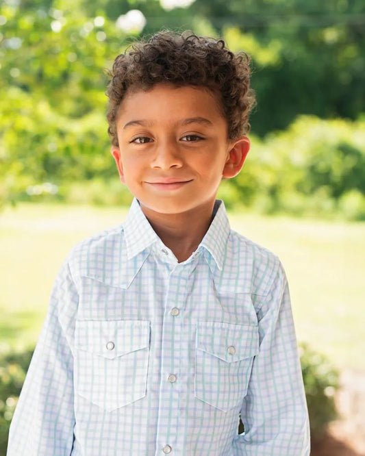 Young boy wearing a light blue checkered shirt outdoors with greenery in the background