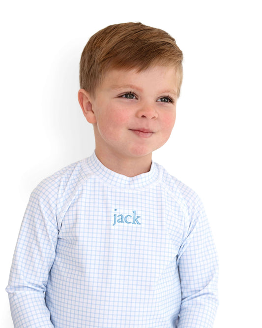Young boy wearing a light blue checkered shirt with 'jack' embroidered on it against a white background