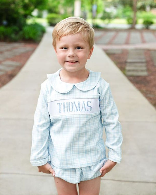 Young boy wearing a light blue outfit with 'THOMAS' printed on it, standing outdoors.