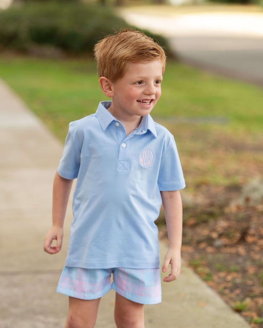 Young boy wearing a light blue polo shirt and plaid shorts outdoors on a path.