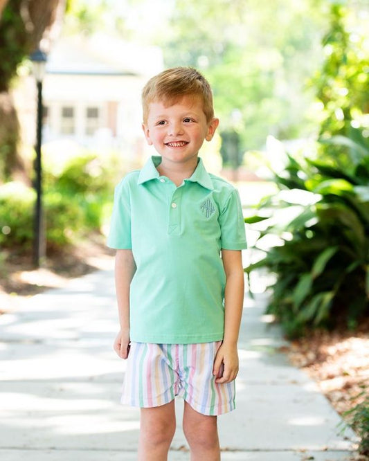 Young boy wearing a light green polo shirt and striped shorts standing outdoors.