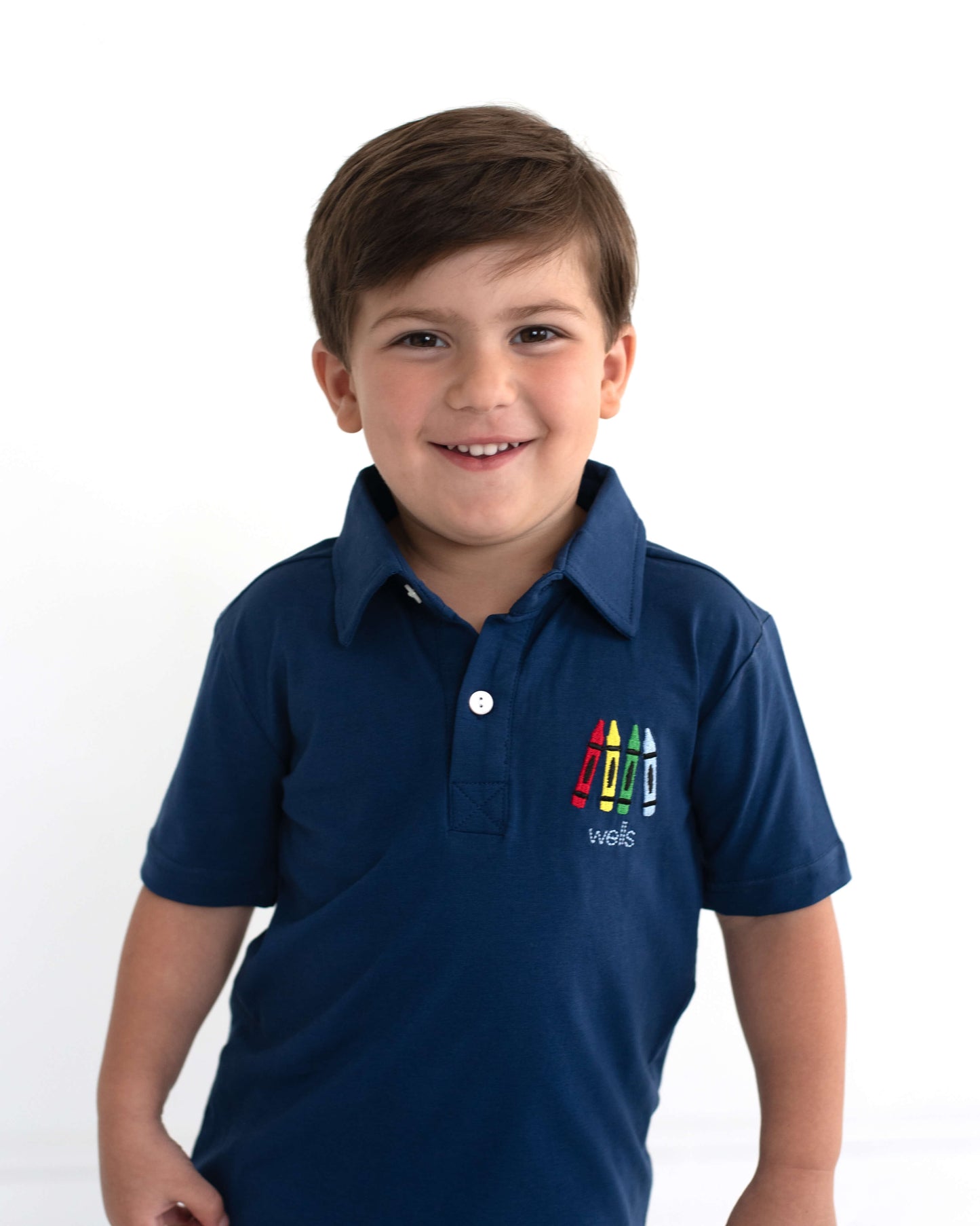 Young boy wearing a navy shirt with crayons and his name embroidered.