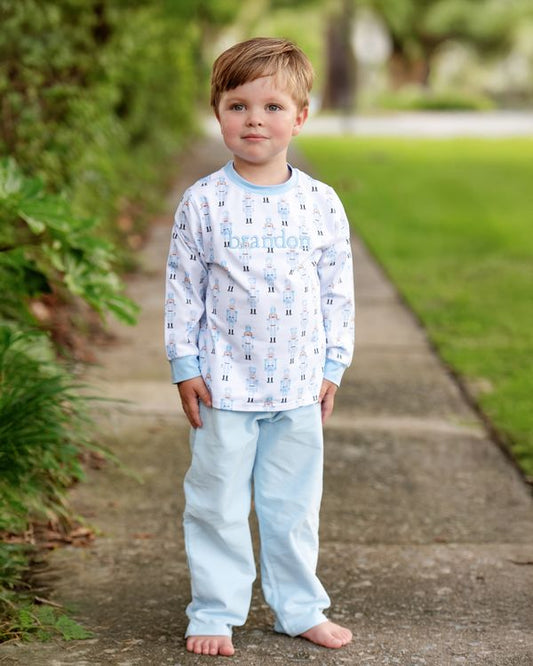 Young boy wearing a patterned long-sleeve shirt and light blue pants standing on a path with greenery.