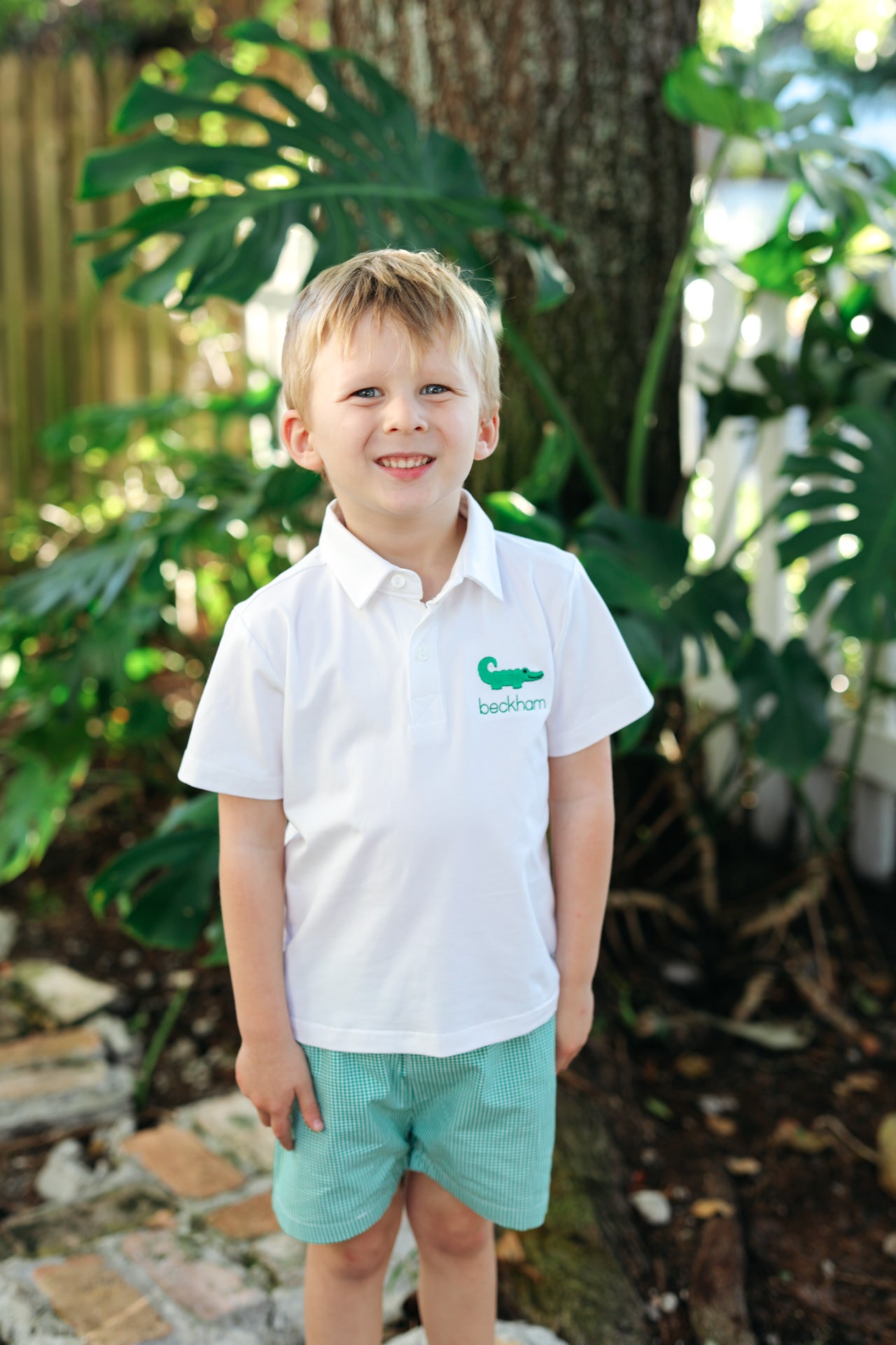 Young boy wearing a polo short set with an embroidered alligator on the chest, standing outside