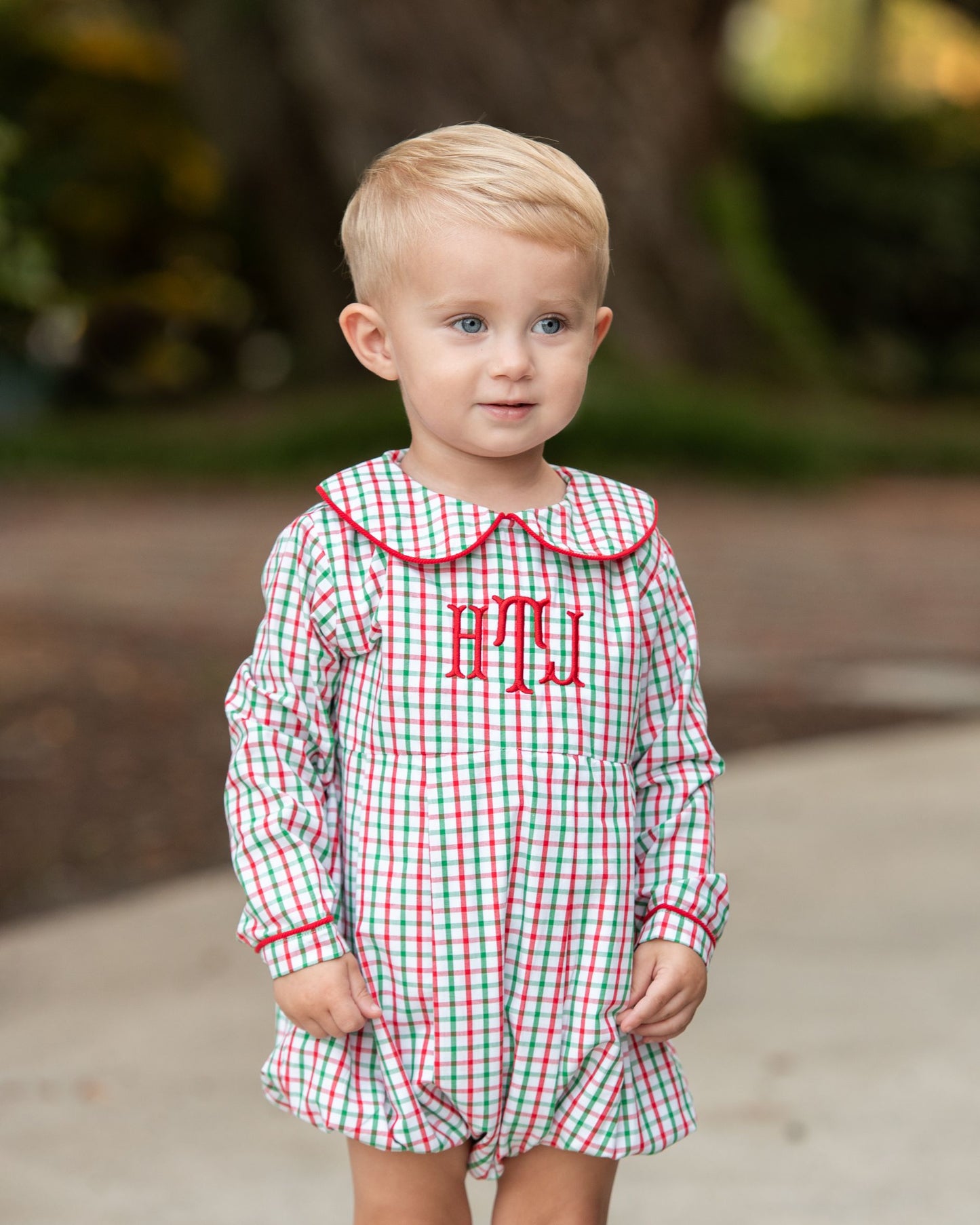 Young boy wearing a red and green checked shirt with matching red corduroy pants, standing on a sidewalk