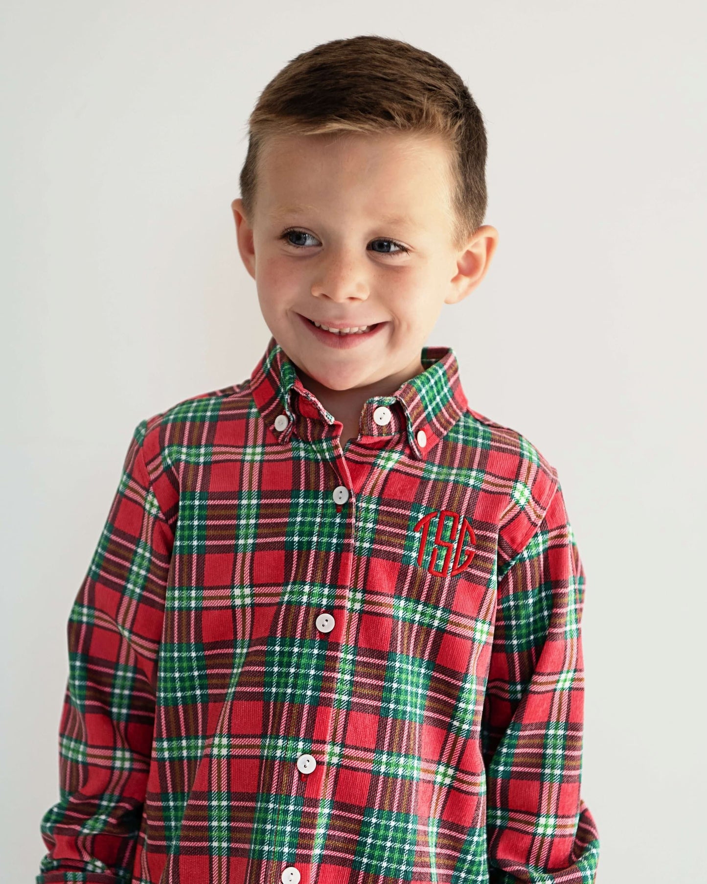 Young boy wearing a red and green plaid shirt with a monogram on a white background