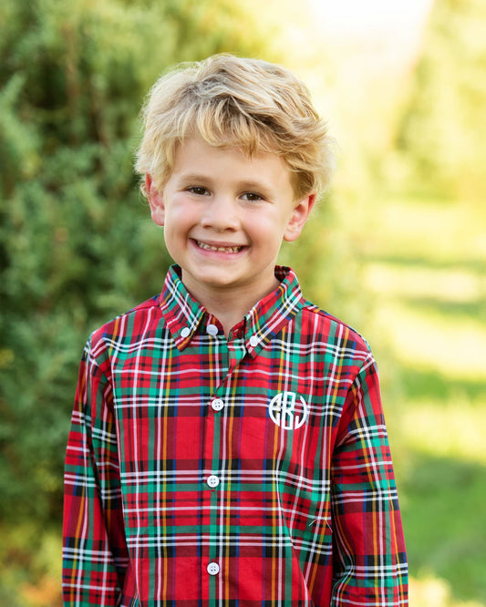Young boy wearing a red plaid shirt with a monogram, standing outdoors.