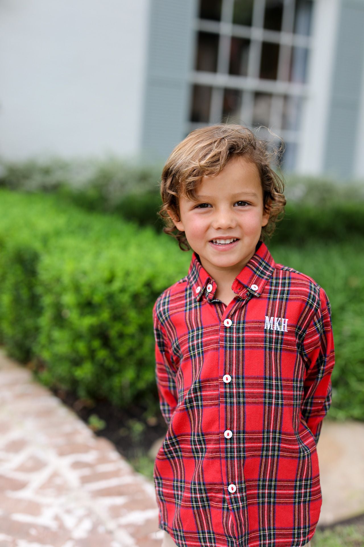 Young boy wearing a red plaid shirt with initials 'MKH' on it, standing outdoors.