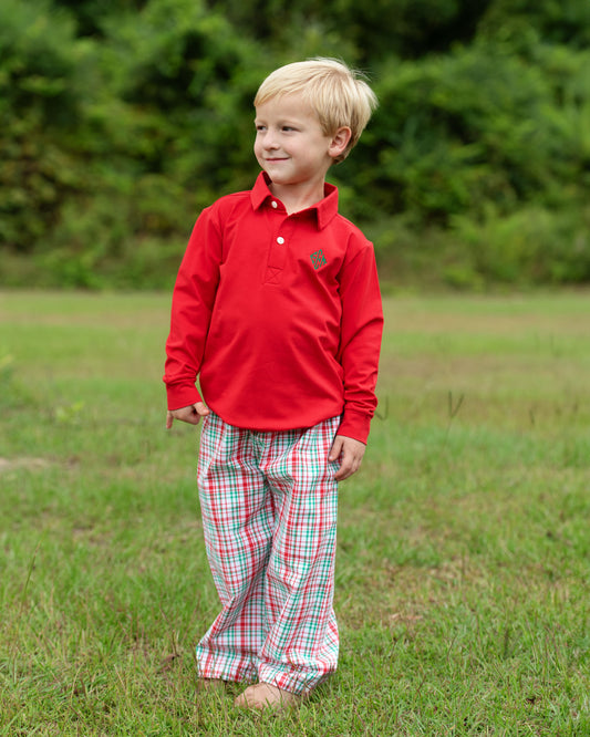 Young boy wearing a red shirt and plaid pants standing in a grassy field.