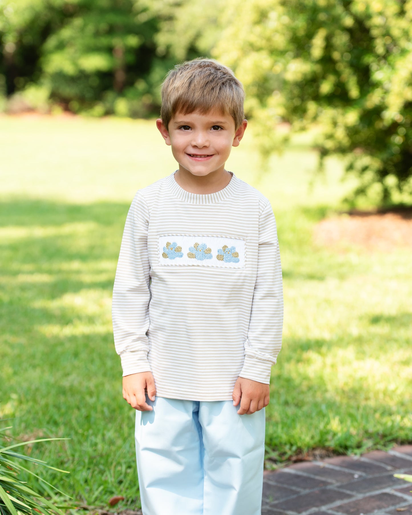 Young boy wearing a striped shirt with a floral design outdoors on a sunny day.