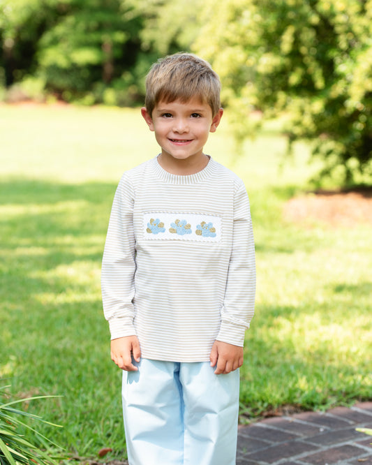 Young boy wearing a striped shirt with a floral design outdoors on a sunny day.