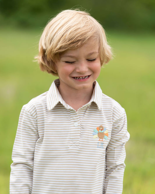 Young boy wearing a striped shirt with a small logo, standing outdoors.