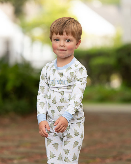Young boy wearing a white onesie with green tree patterns outdoors.