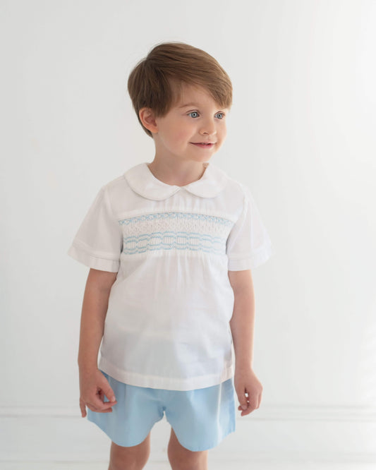 Young boy wearing a white shirt with a collar and light blue shorts on a white background