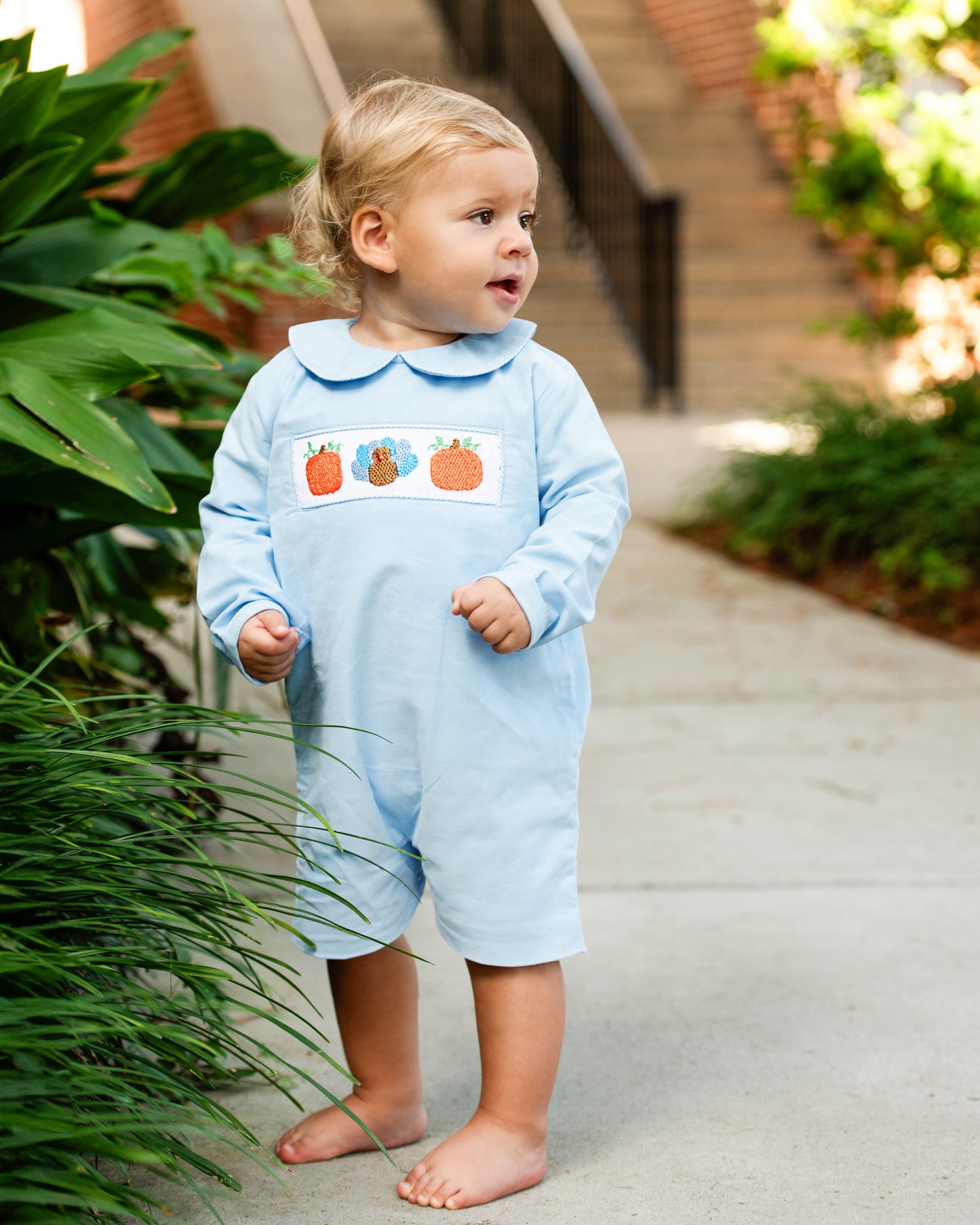 Young boy wearing blue short romper with smocked pumpkins and a turkey