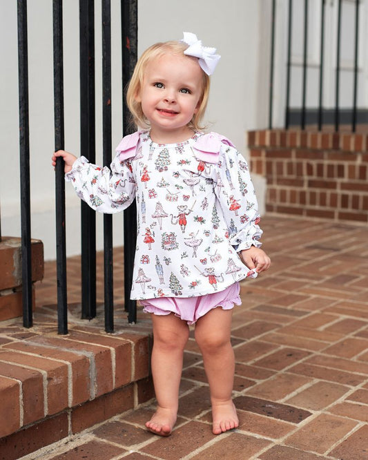 Young child standing on a brick patio wearing a patterned jacket and pink shorts.