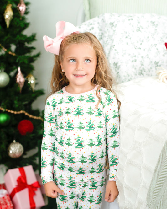 Young girl in Christmas-themed pajamas standing in front of a decorated Christmas tree with presents.