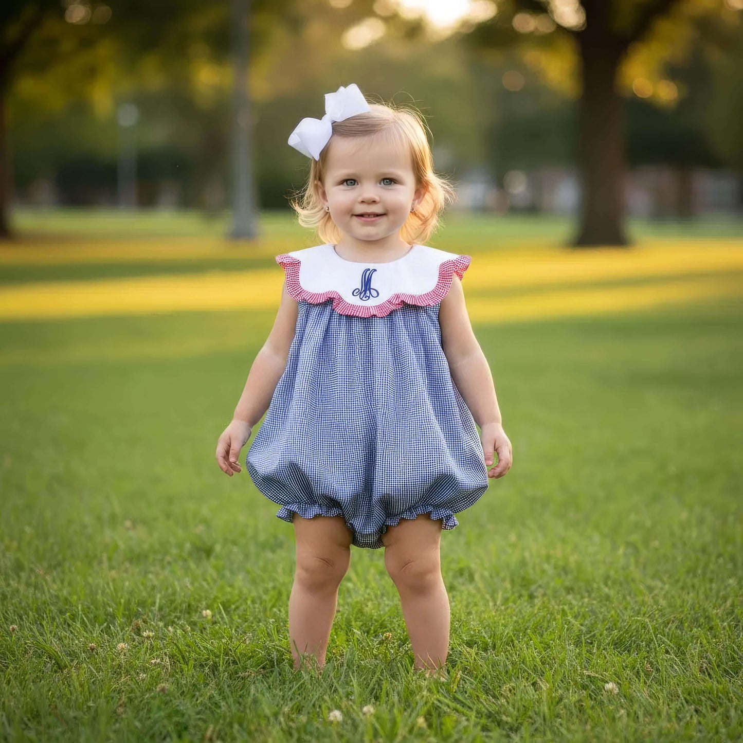 Young girl in a blue checkered dress with a white bow standing on grass