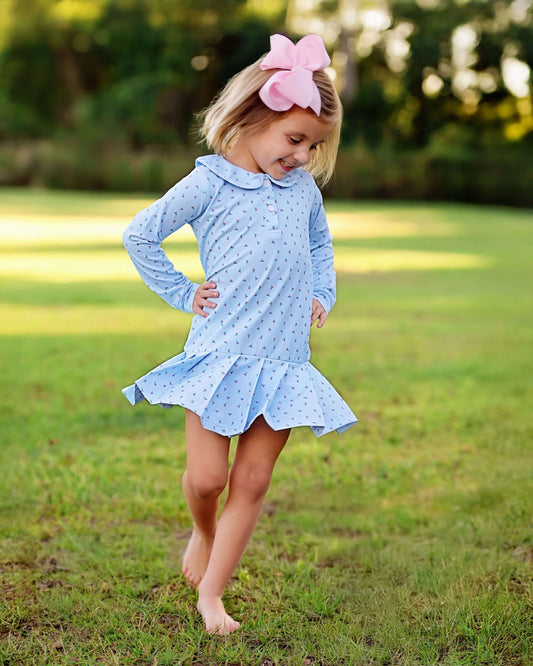 Young girl in a blue dress with a pink bow standing on grass