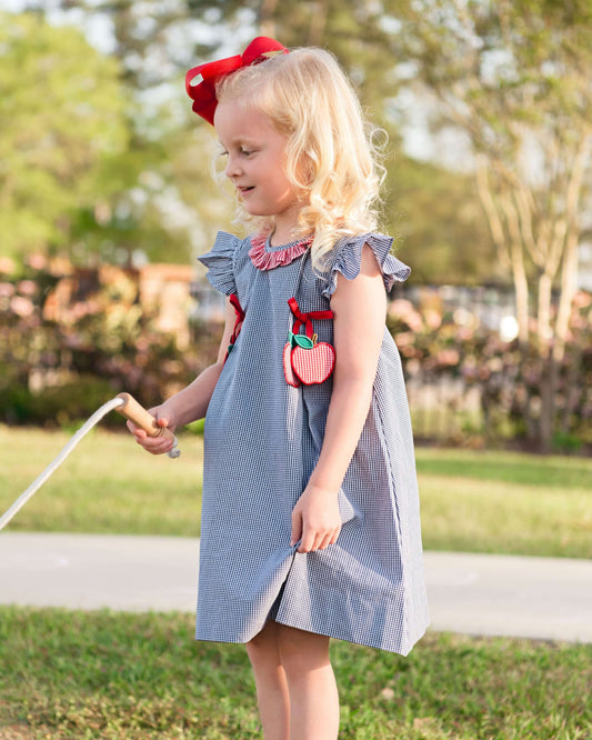 Young girl in a blue dress with red accents standing outdoors.