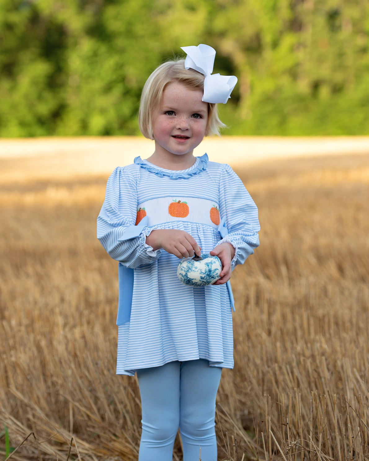 Young girl in a blue legging set with pumpkin design standing in a field.