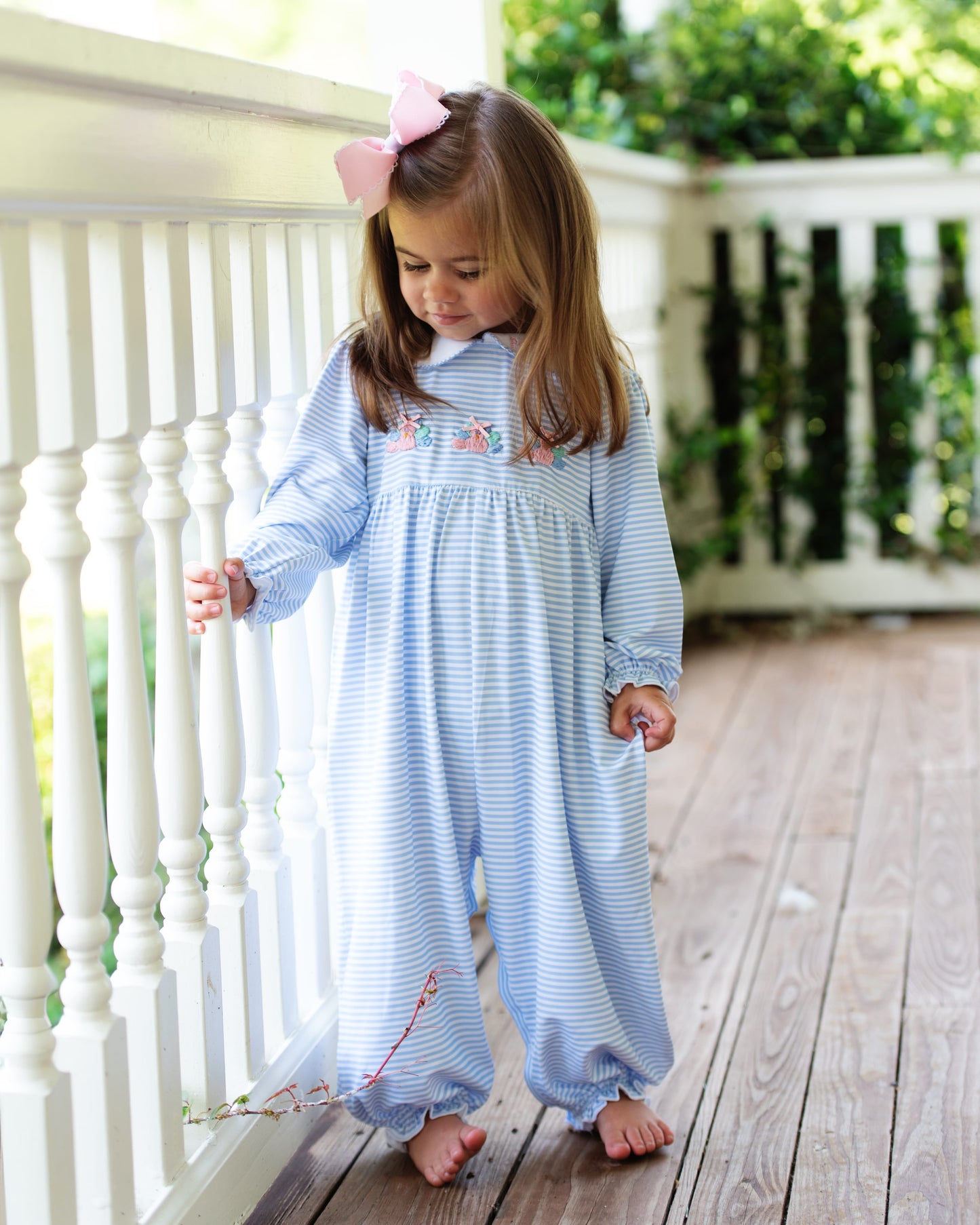 Young girl in a blue striped long bubble with turkeys standing on a wooden deck.