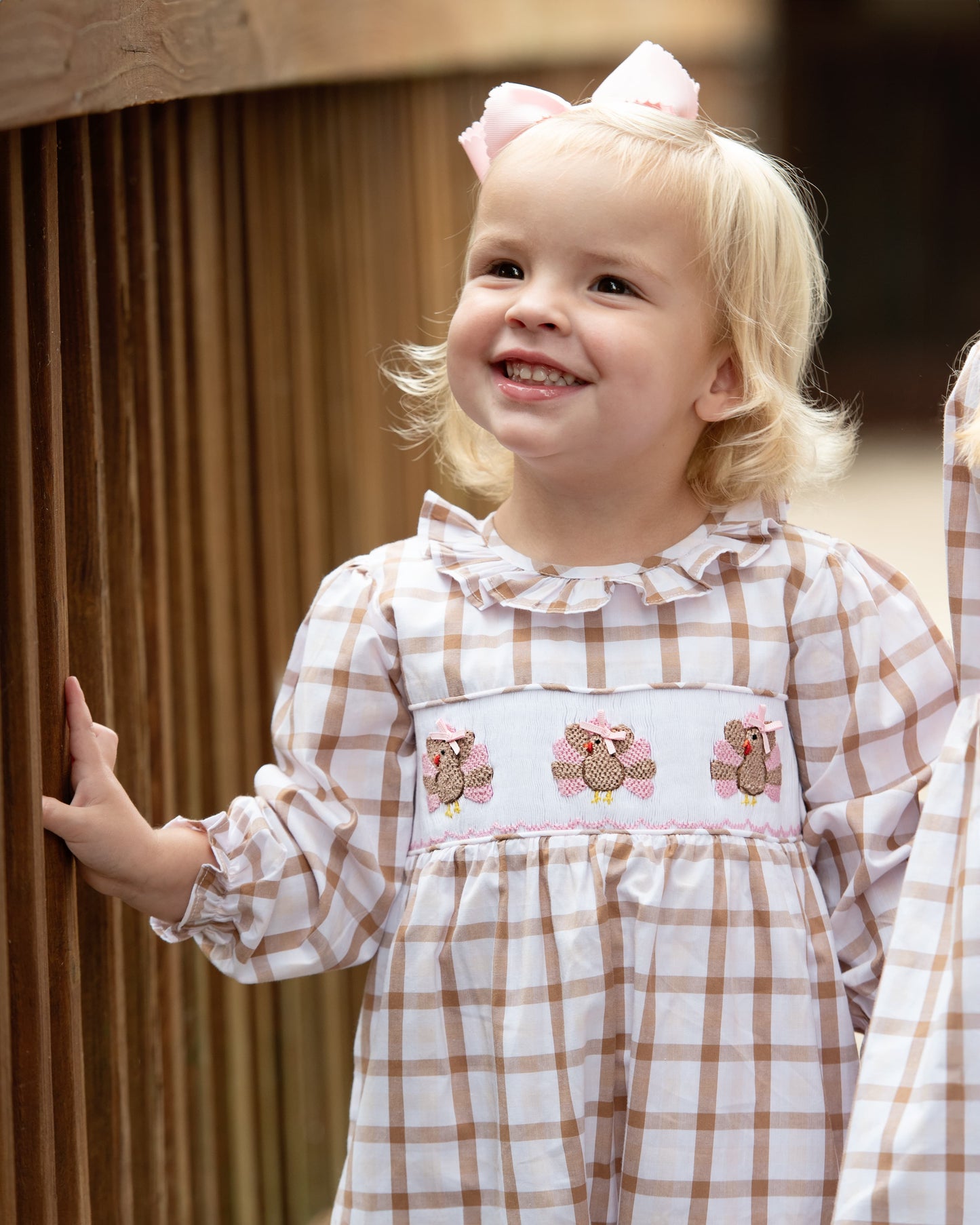 Young girl in a checkered dress with turkeys designs, standing indoors.