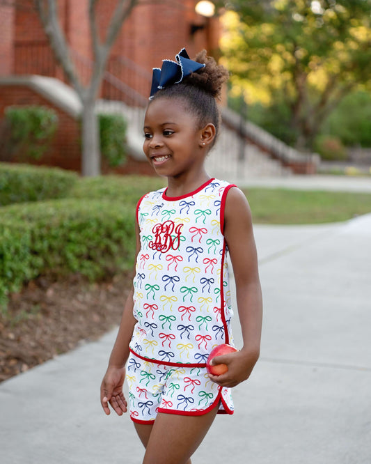 Young girl in a colorful bow-patterned outfit with a red trim, standing outdoors.
