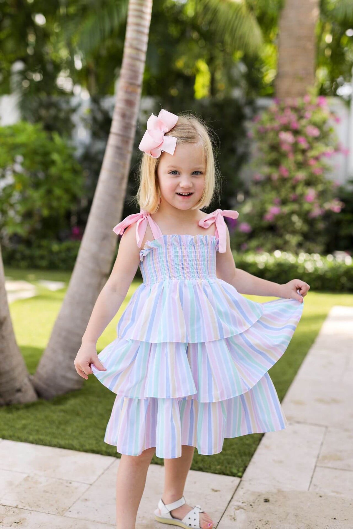 Young girl in a colorful dress standing outdoors with palm trees and flowers in the background