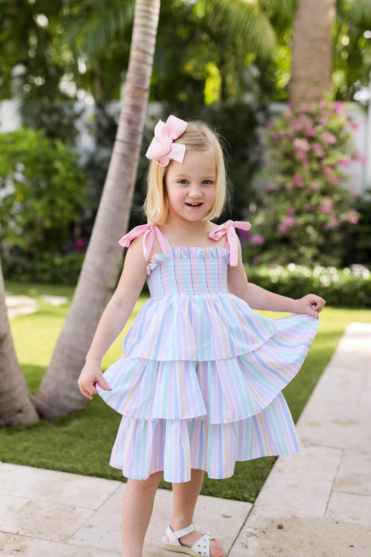 Young girl in a colorful dress standing outdoors with palm trees and flowers in the background