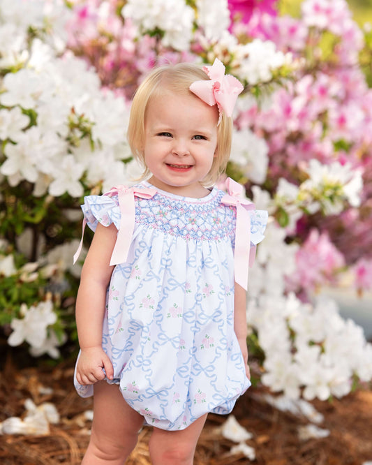 Young girl in a floral bubble standing in front of flowering bushes.