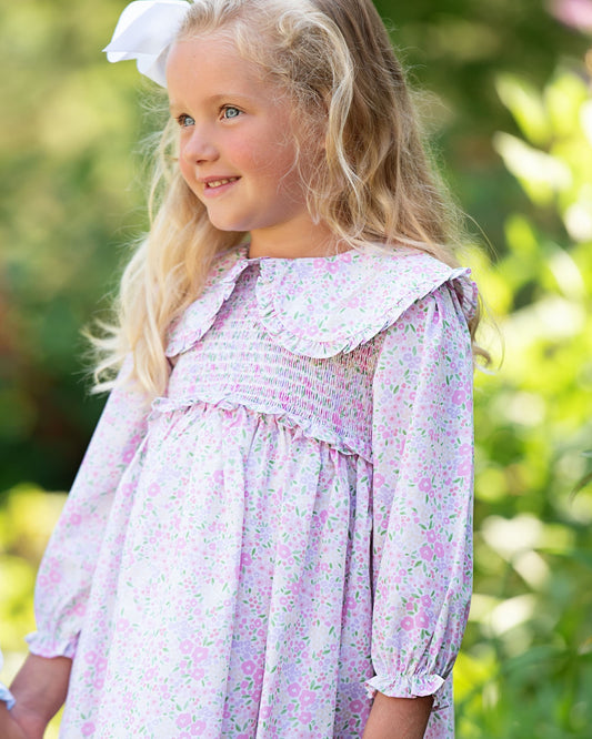 Young girl in a floral dress standing outdoors with a blurred green background
