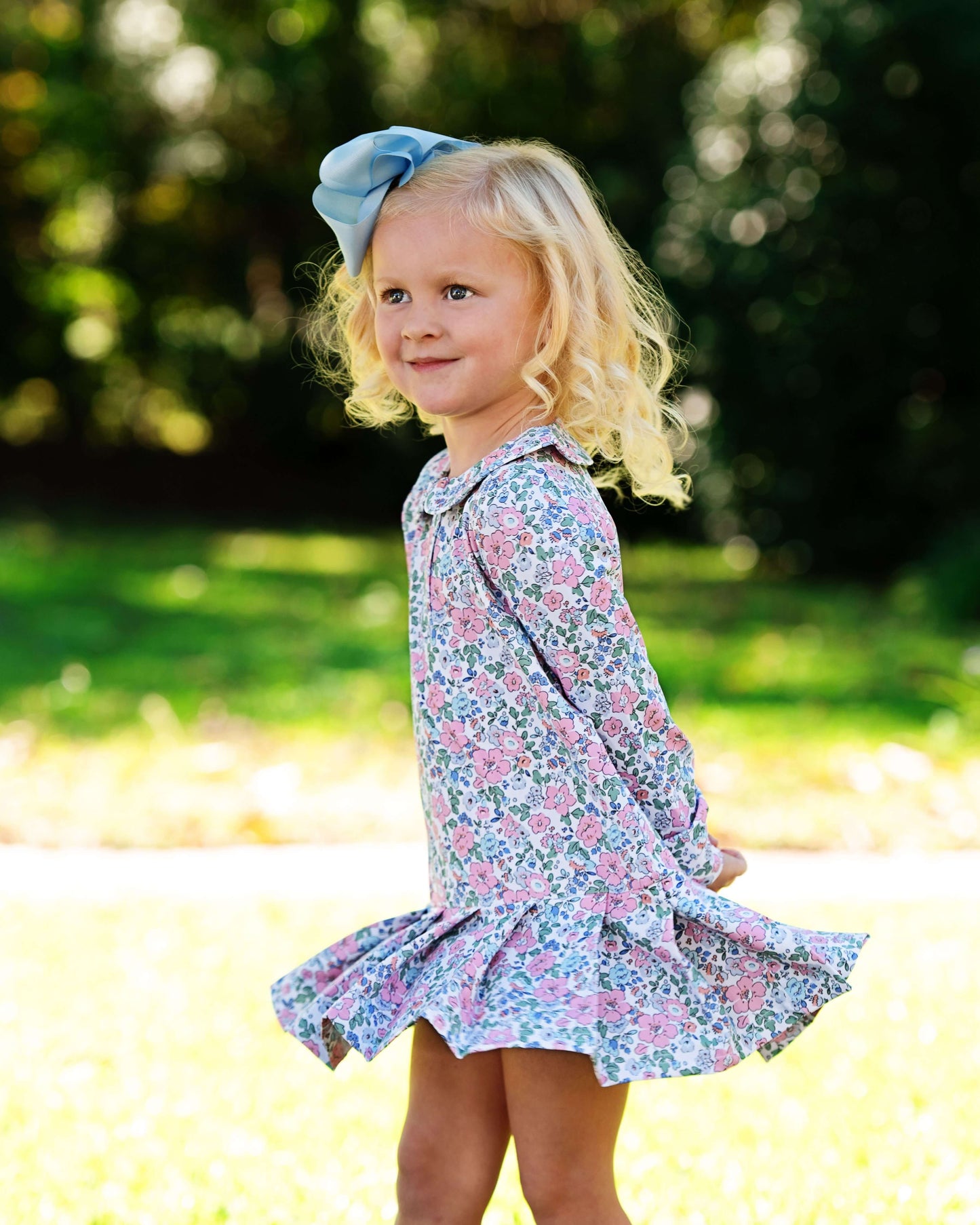 Young girl in a floral dress with a blue bow outdoors