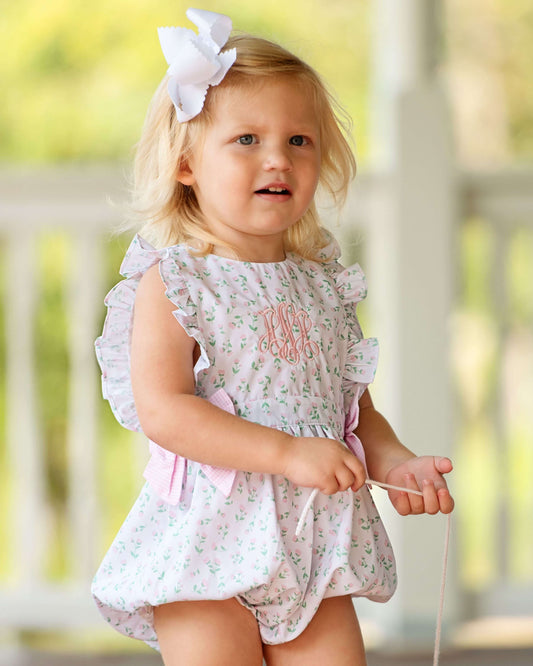 Young girl in a floral dress with a bow, standing outdoors.